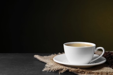 Cup of hot aromatic coffee and roasted beans on black table against dark background, space for text