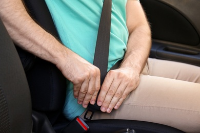 Photo of Man fastening safety belt on driver's seat in car, closeup