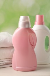 Photo of Bottles of laundry detergents and clean clothes on white wooden table