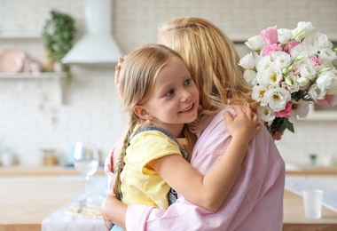 Cute little girl with bouquet hugging her grandmother in kitchen. Space for text