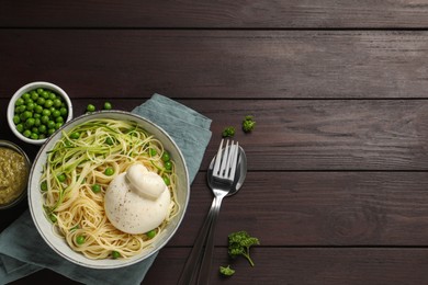 Bowl of delicious pasta with burrata, peas and zucchini served on wooden table, flat lay. Space for text