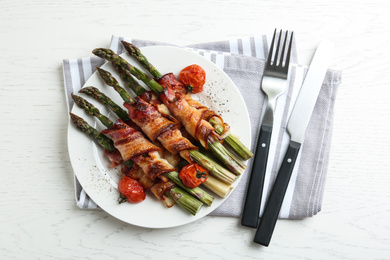 Oven baked asparagus wrapped with bacon on white wooden table, flat lay
