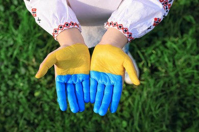 Little girl with hands painted in Ukrainian flag colors outdoors, top view. Love Ukraine concept