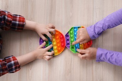 Little children playing with pop it fidget toys at wooden table, top view