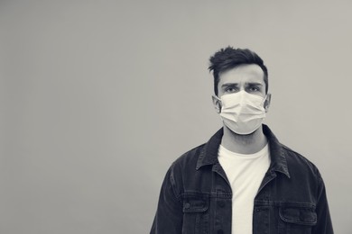 Man wearing medical face mask on light background, space for text. Black and white photography
