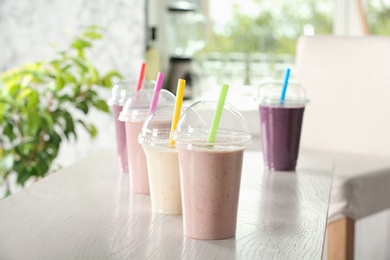 Different milk shakes in plastic cups on white wooden table indoors
