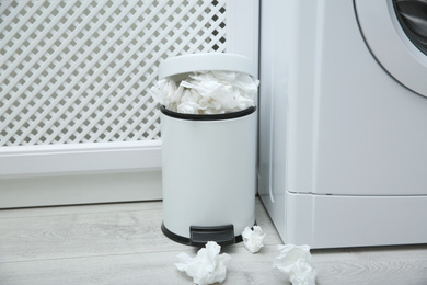 Used paper tissues in trash can near washing machine indoors