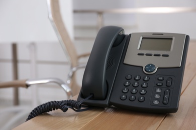 Desktop telephone on wooden table in office, space for text. Hotline service