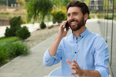 Photo of Handsome man talking on phone outdoors, space for text