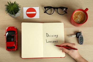 Woman with workbook for driving lessons and cup of coffee at white wooden table, top view. Passing license exam