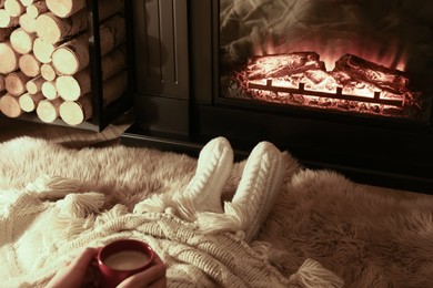 Photo of Woman with hot drink resting near fireplace at home, closeup