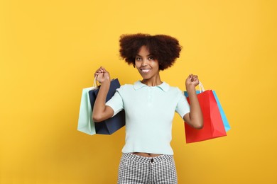 Photo of Happy African American woman with shopping bags on orange background
