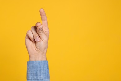 Man snapping fingers on yellow background, closeup of hand. Space for text