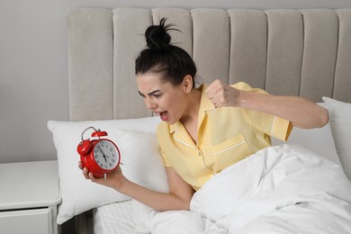 Emotional overslept woman with alarm clock in bed. Being late concept