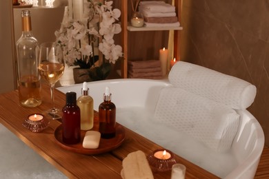 Tub with soft bath pillow, toiletries and wine indoors