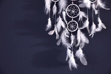 Beautiful dream catcher hanging on dark blue wall, closeup. Space for text