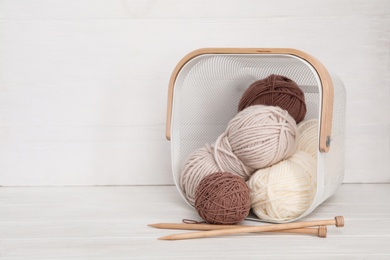 Woolen yarns in basket and knitting needles on white wooden table. Space for text