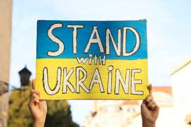 Woman holding poster Stand with Ukraine outdoors, closeup
