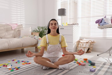 Photo of Calm young mother meditating on floor in messy living room