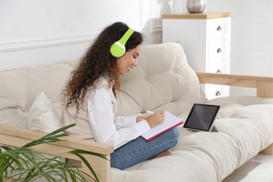African American woman with notebook and headphones studying on sofa at home. Distance learning