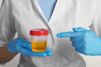 Photo of Nurse holding container with urine sample for analysis on white background, closeup