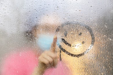 Woman drawing happy face on foggy window at rainy weather, closeup