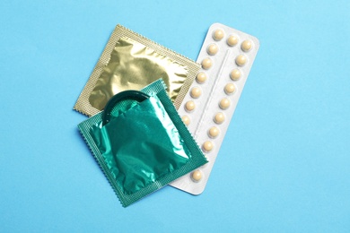 Condoms and birth control pills on light blue background, flat lay. Safe sex concept