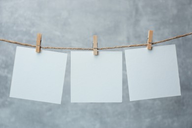 Wooden clothespins with blank notepapers on twine against grey background. Space for text