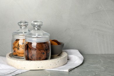 Delicious chocolate chip cookies in glass jars on light grey marble table, space for text