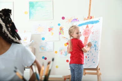 Cute little child painting on easel at lesson indoors