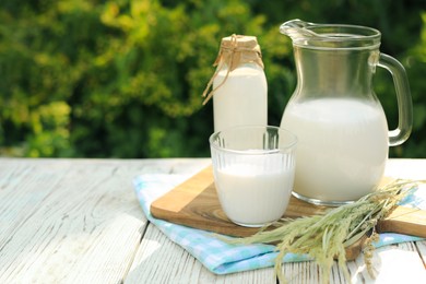 Jug, bottle and glass of tasty fresh milk on white wooden table outdoors, space for text