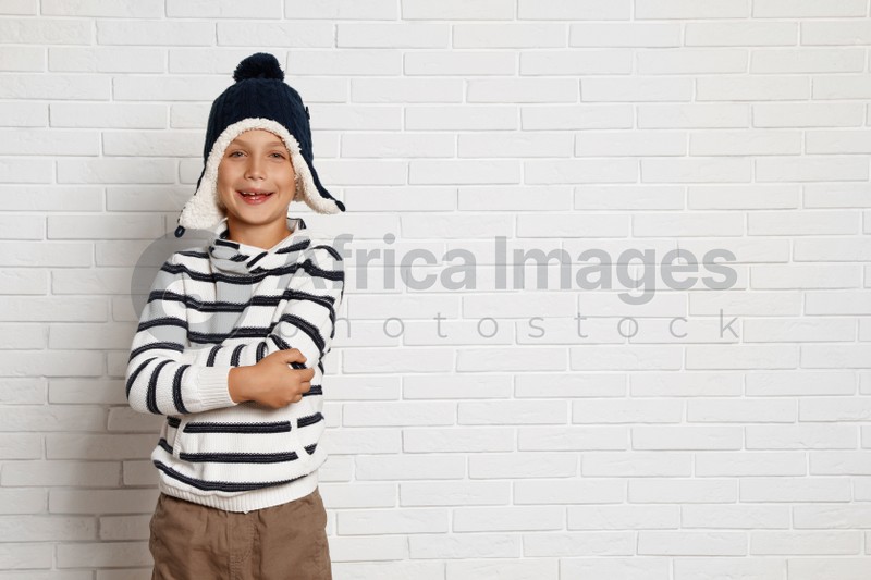 Cute little boy in hat and sweater near white brick wall, space for text. Winter season