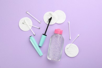 Dirty cotton pads, swabs, mascara and micellar cleansing water on lilac background, flat lay