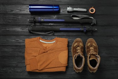 Flat lay composition with trekking poles and other hiking equipment on black wooden background