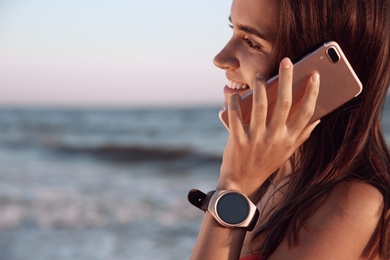 Young woman with smart watch talking on phone at beach, closeup