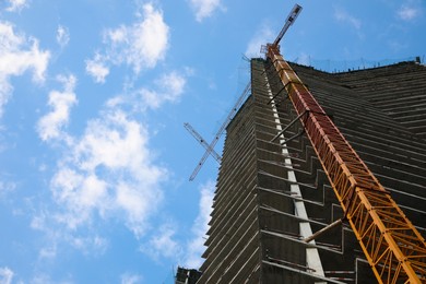 Construction site with tower crane near unfinished building under cloudy sky, low angle view