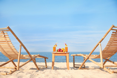 Wooden deck chairs near table with fruits and drinks on beach