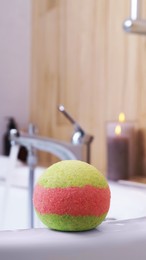 Photo of Colorful bath bomb on white tub in bathroom