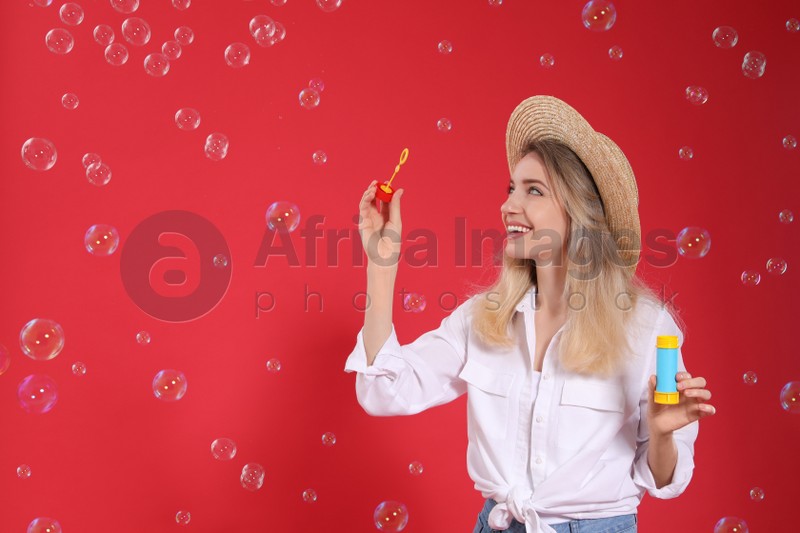 Young woman blowing soap bubbles on red background, space for text