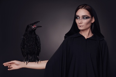 Mysterious witch with raven on dark background