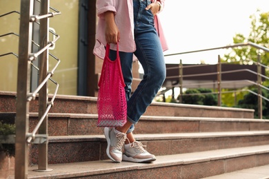 Young woman with stylish pink net bag on stairs outdoors, closeup
