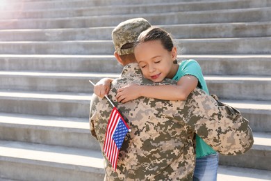 Soldier and his little daughter with flag of USA hugging outdoors, space for text