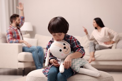 Sad little boy with toy and his arguing parents on sofa in living room