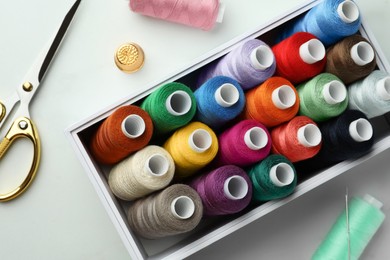 Photo of Box with colorful sewing threads, scissors and thimble on white marble table, flat lay