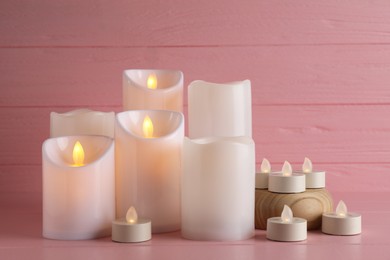 Glowing decorative LED candles on pink wooden background