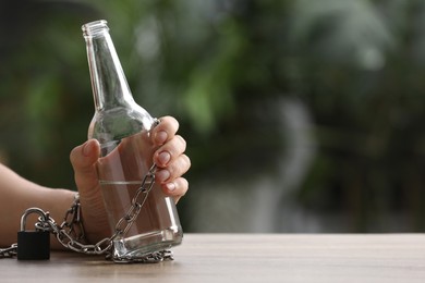 Man chained to bottle of vodka at table against blurred background, closeup with space for text. Alcohol addiction