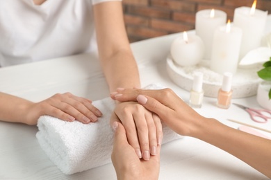 Cosmetologist massaging client's hand at table in spa salon, closeup