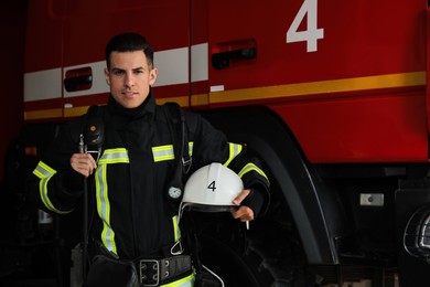 Portrait of firefighter in uniform with helmet near fire truck at station, space for text