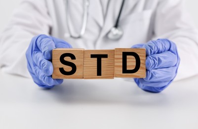Doctor holding wooden cubes with abbreviation STD at white table, closeup