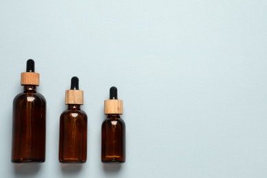 Bottles of face serum on light grey background, flat lay. Space for text